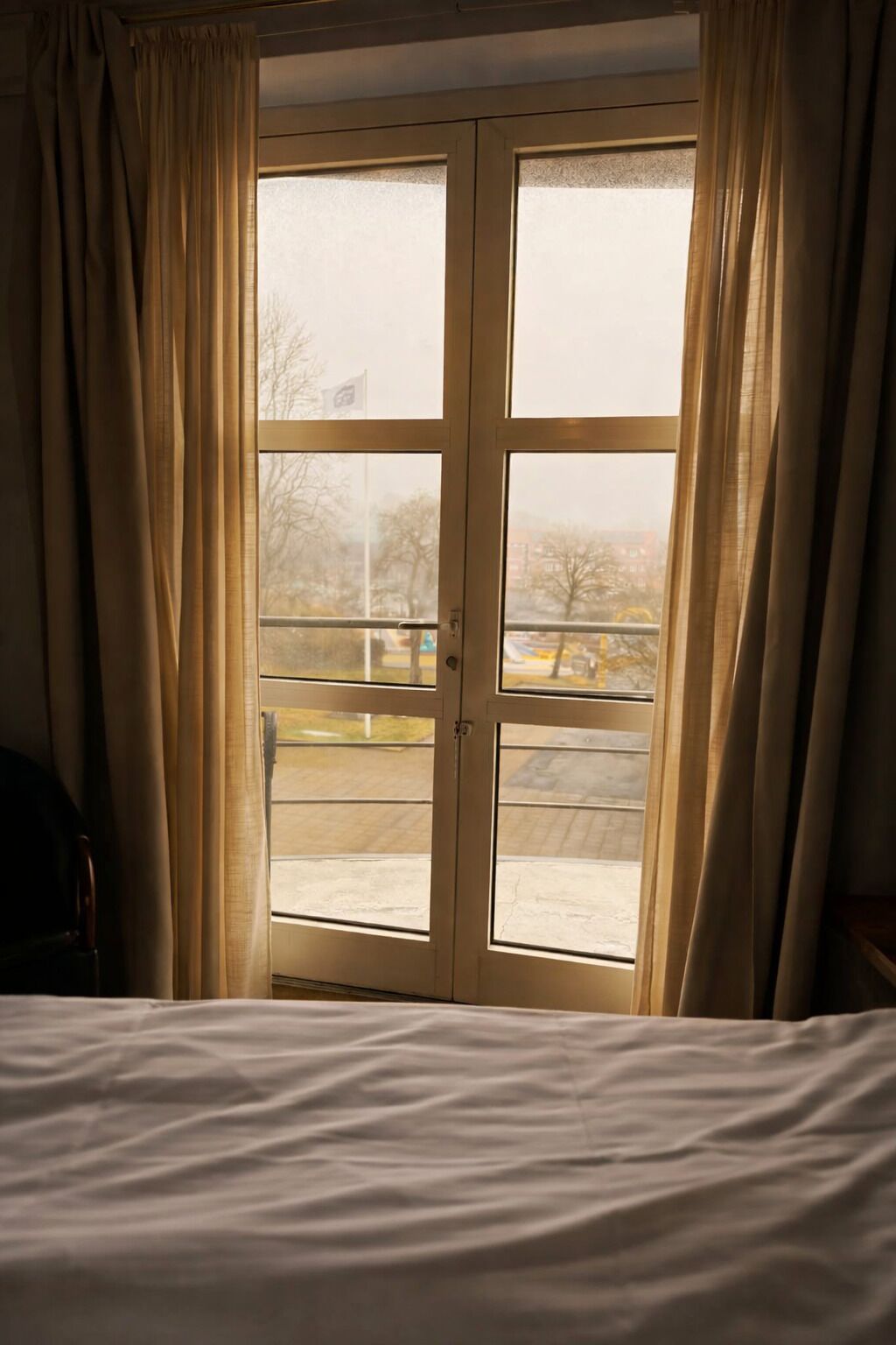 Una habitación con cama, ventana con cortinas y vista a un estacionamiento.
