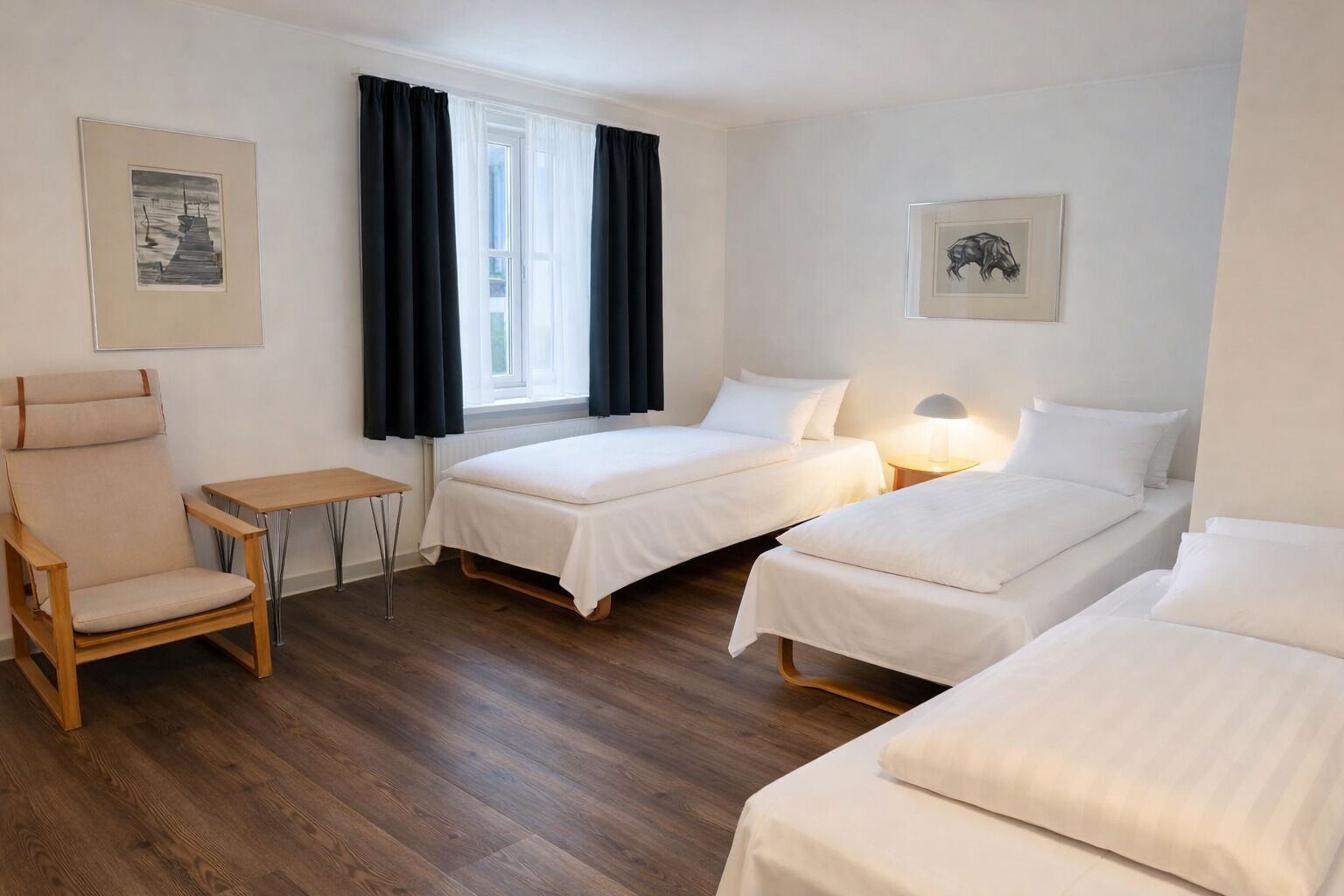 Una habitación con dos camas, una silla, una mesita, una ventana con cortinas y obras de arte en las paredes.