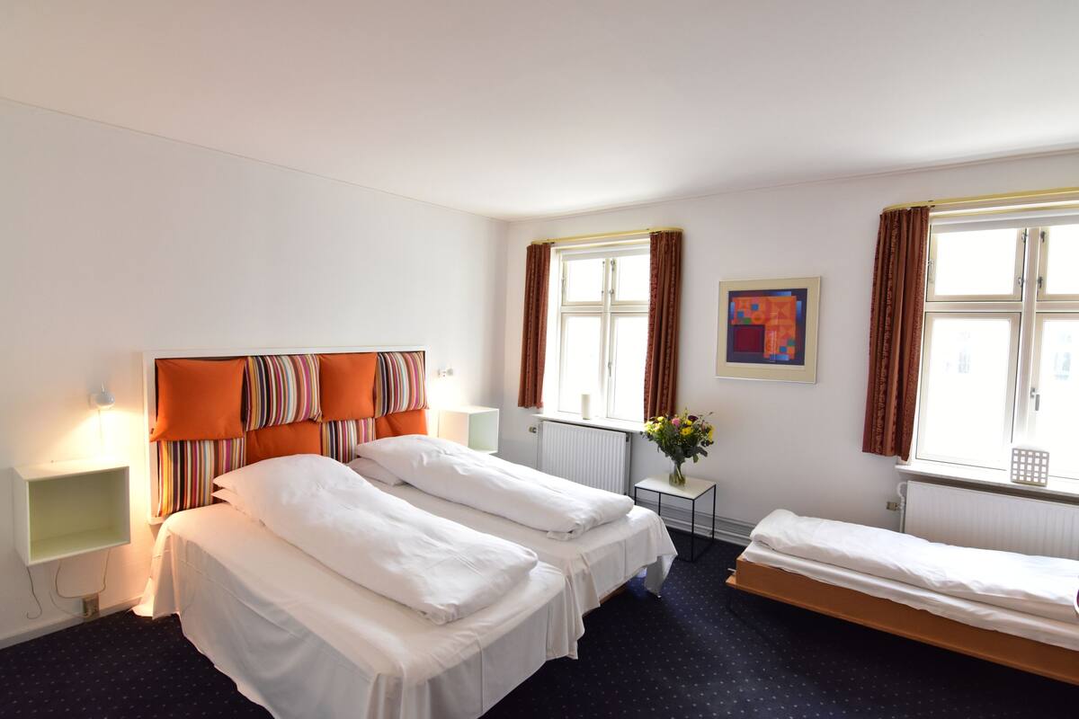 Een hotelkamer met twee bedden, een tafeltje met een vaas en een raam met gordijnen.