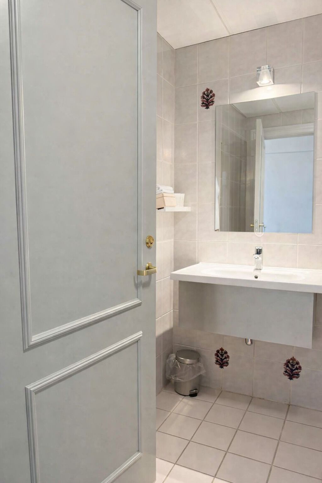 A bathroom with a white sink, a mirror, and a trash bin.