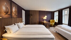 Een hotelkamer met twee bedden, een bureau, een stoel en kunstwerken aan de muren.