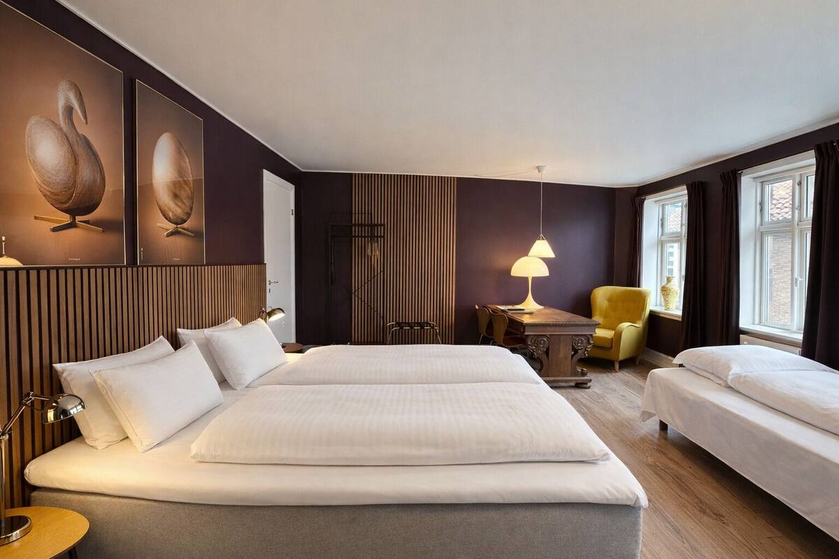 Een hotelkamer met twee bedden, een bureau, een stoel en kunstwerken aan de muren.