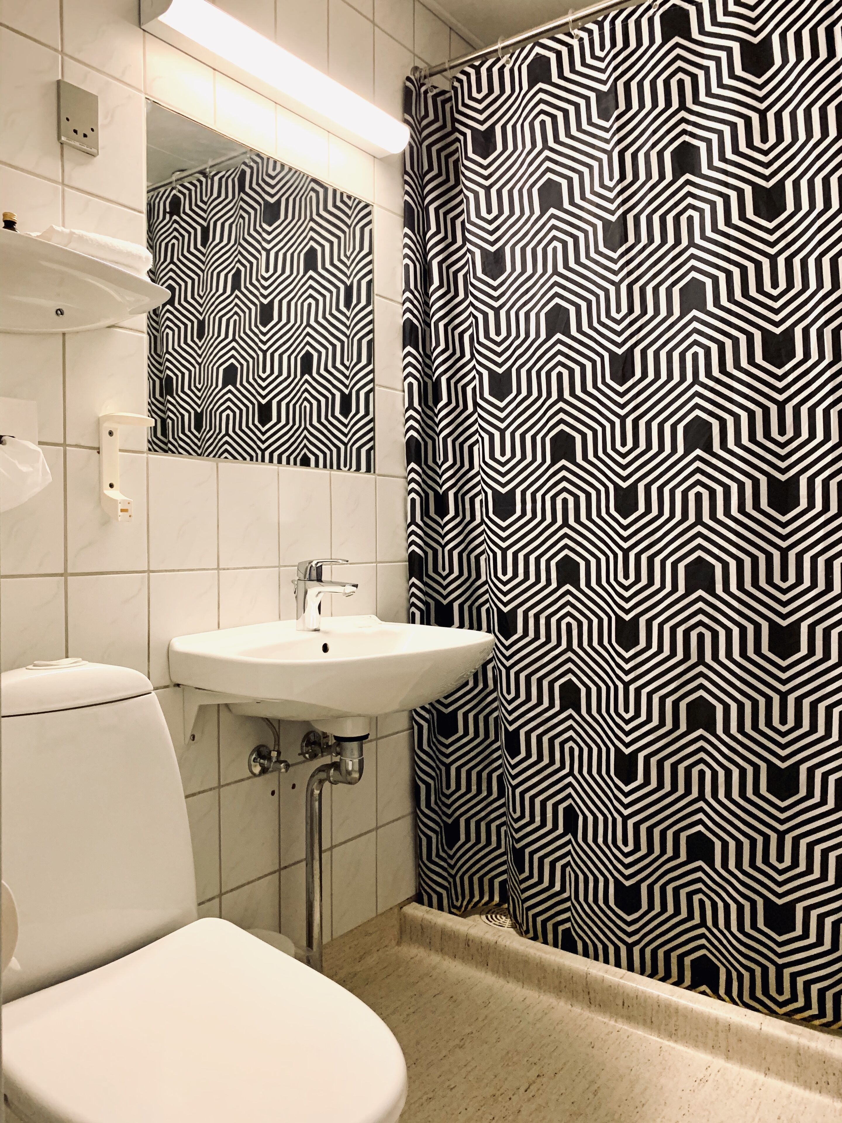A bathroom with a white toilet, a white sink, and a mirror above the sink. The walls have a black and white zigzag pattern.