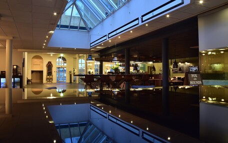 A spacious atrium with a glass ceiling, a bar area, and a seating area with tables and chairs.