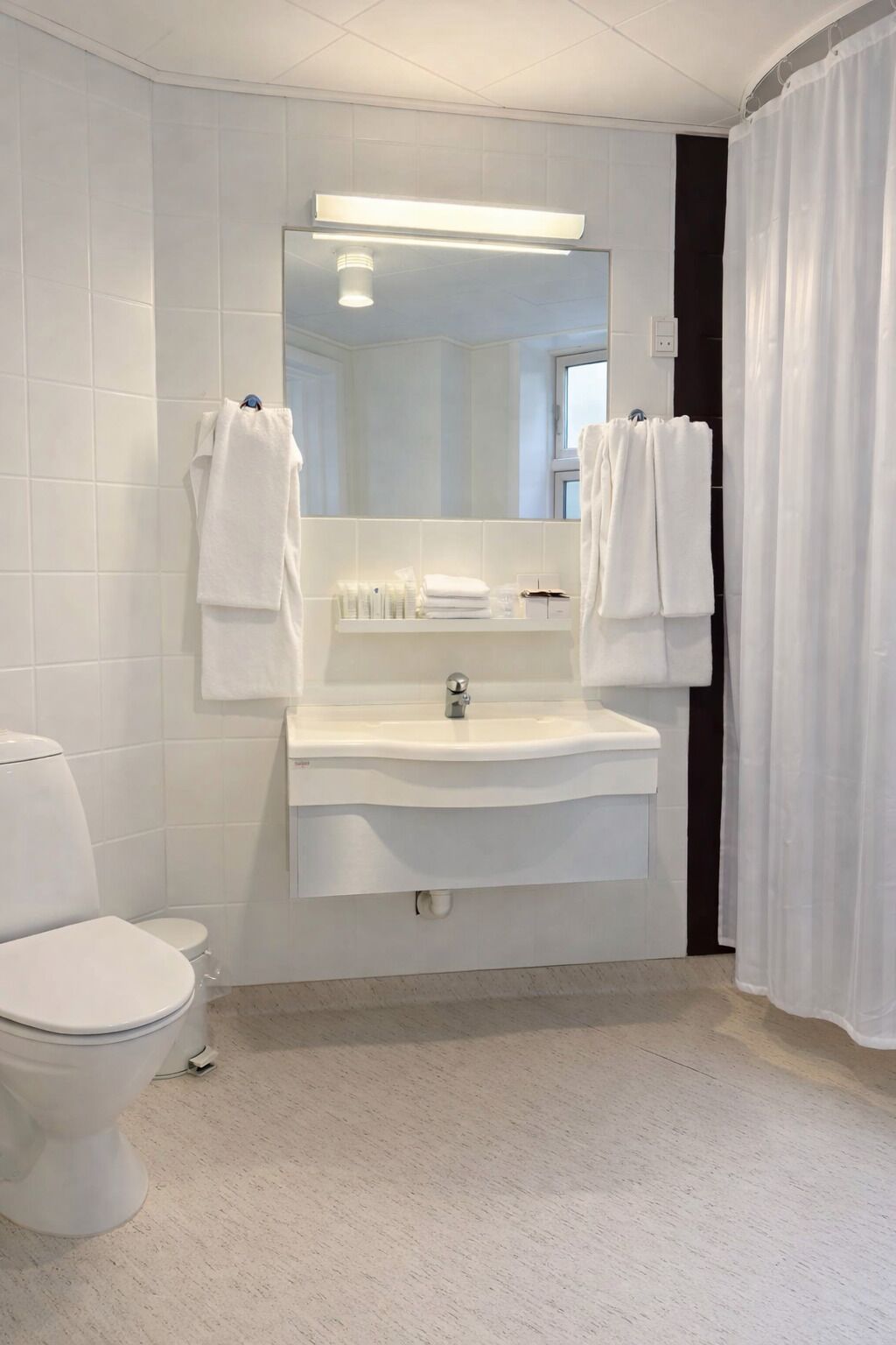 Un baño con un lavamanos blanco, un espejo y dos toallas colgadas de ganchos.
