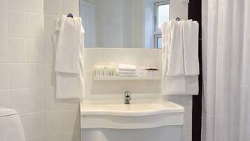 Un baño con un lavamanos blanco, un espejo y dos toallas colgadas de ganchos.