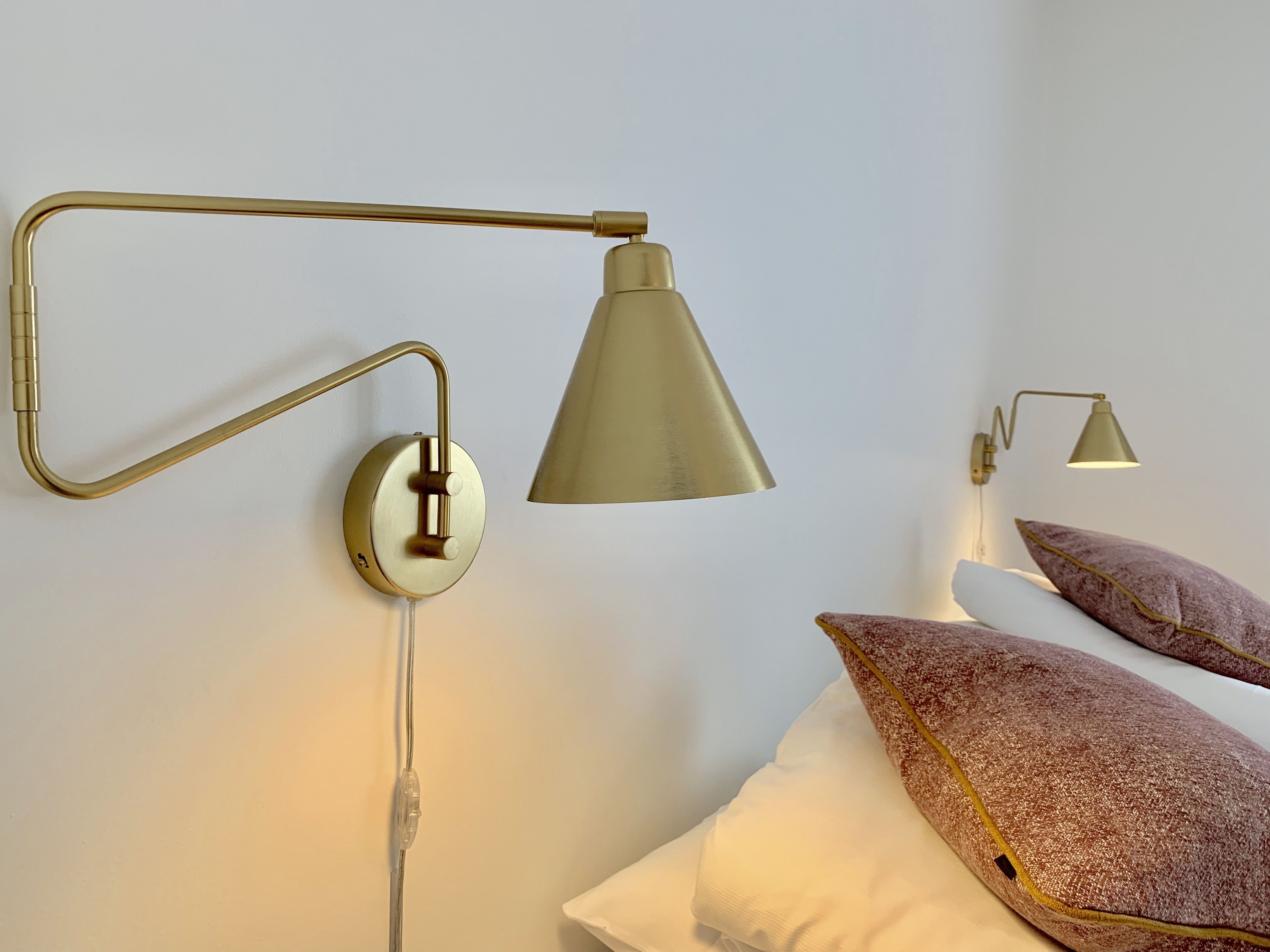 A modern bedroom with a bed, two pillows, and two wall-mounted lamps.