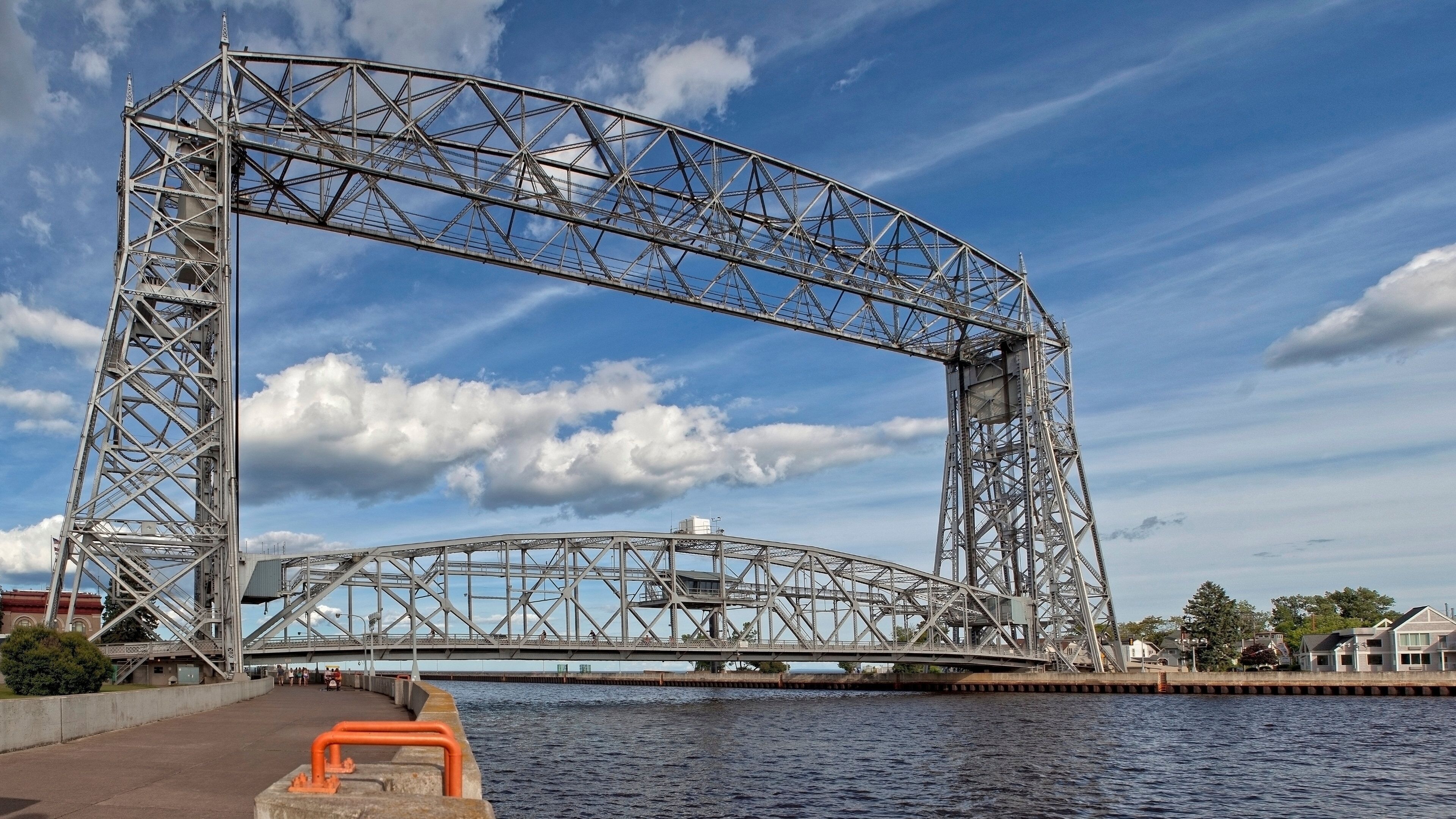A large metal bridge structure over a body of water with a clear sky and some clouds.