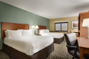 Habitación de hotel con dos camas, un escritorio, una silla y una ventana con vista a la ciudad.