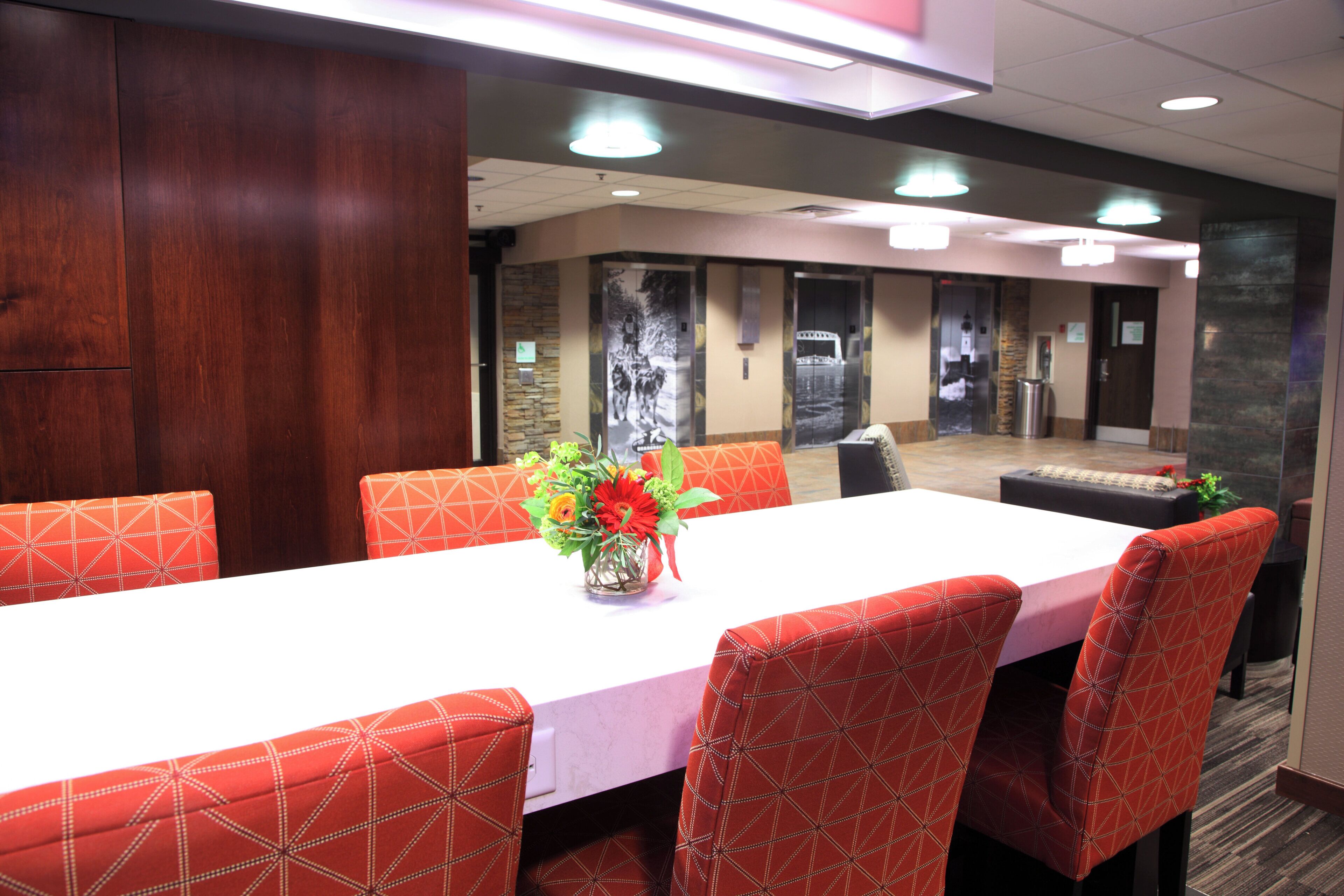 A conference room with a long table, red patterned chairs, and a vase with flowers.
