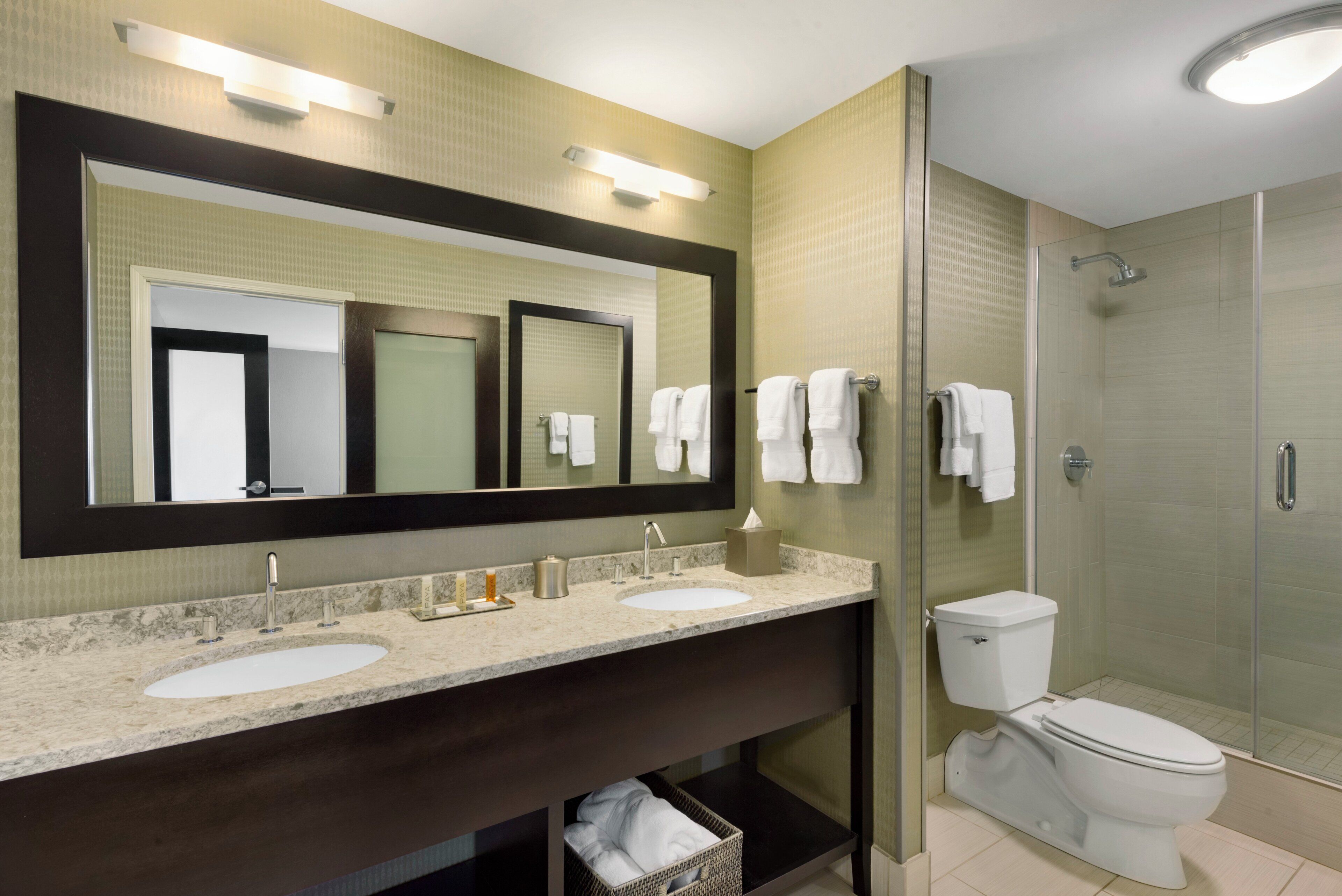 Un baño moderno con un espejo grande, dos lavamanos, un inodoro y una ducha.