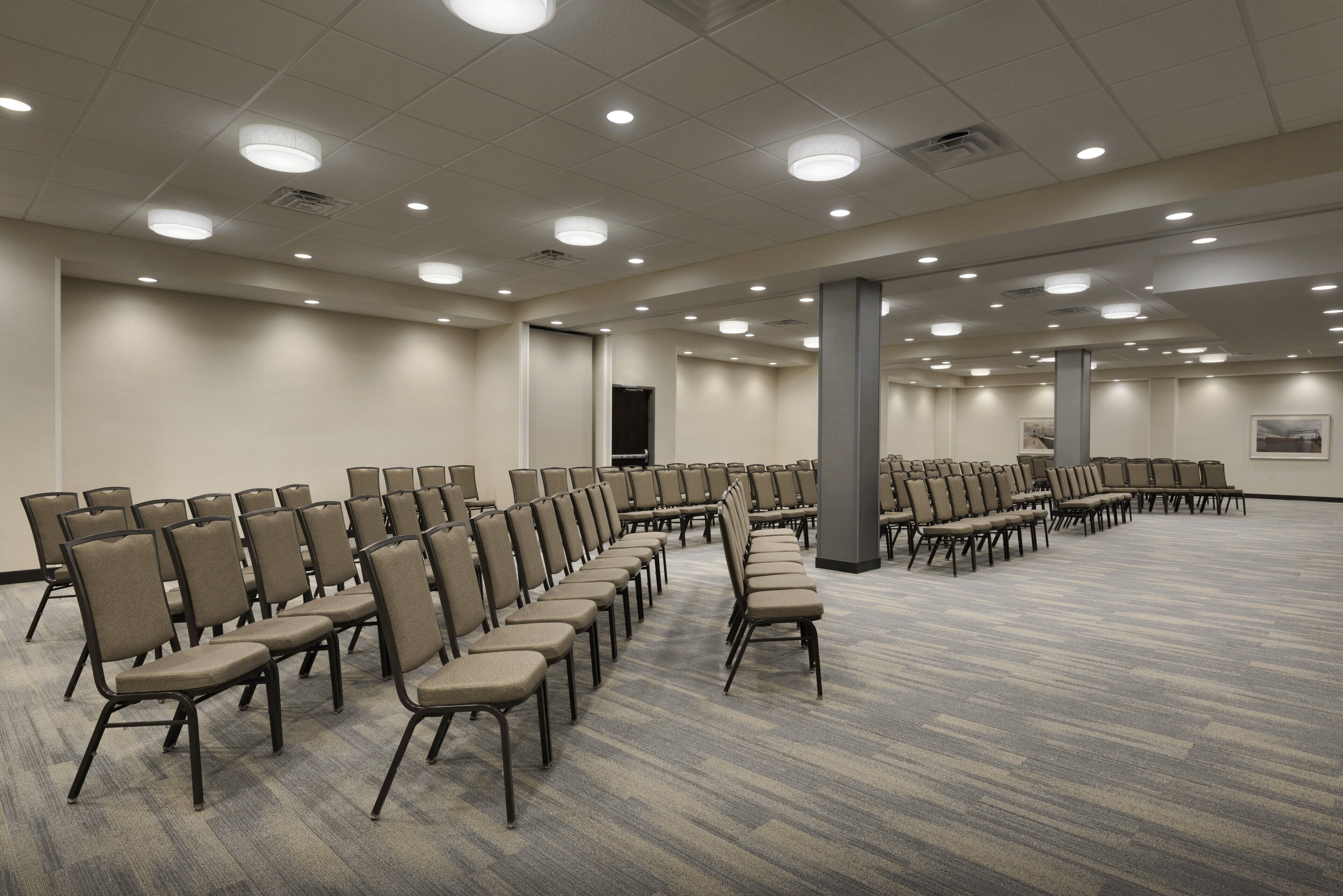 A large conference room with rows of chairs, a stage, and a carpeted floor.