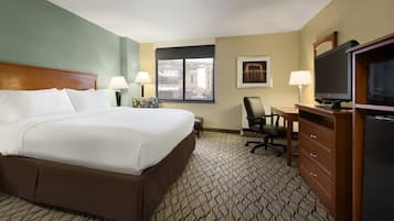 Habitación de hotel con una cama grande, un escritorio con silla, televisión y ventana con vistas a edificios.