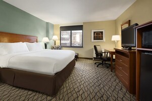 Habitación de hotel con una cama grande, un escritorio con silla, televisión y ventana con vistas a edificios.