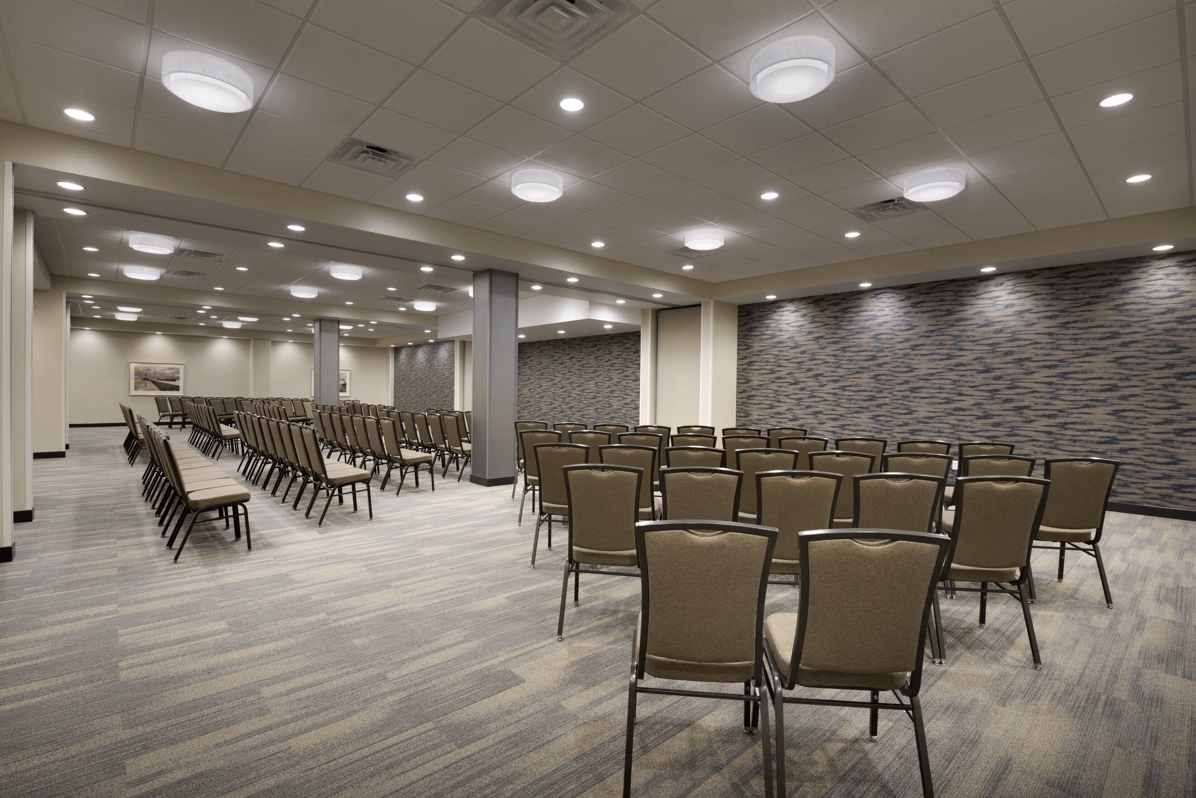 A conference room with rows of chairs, a patterned wall, and recessed ceiling lights.