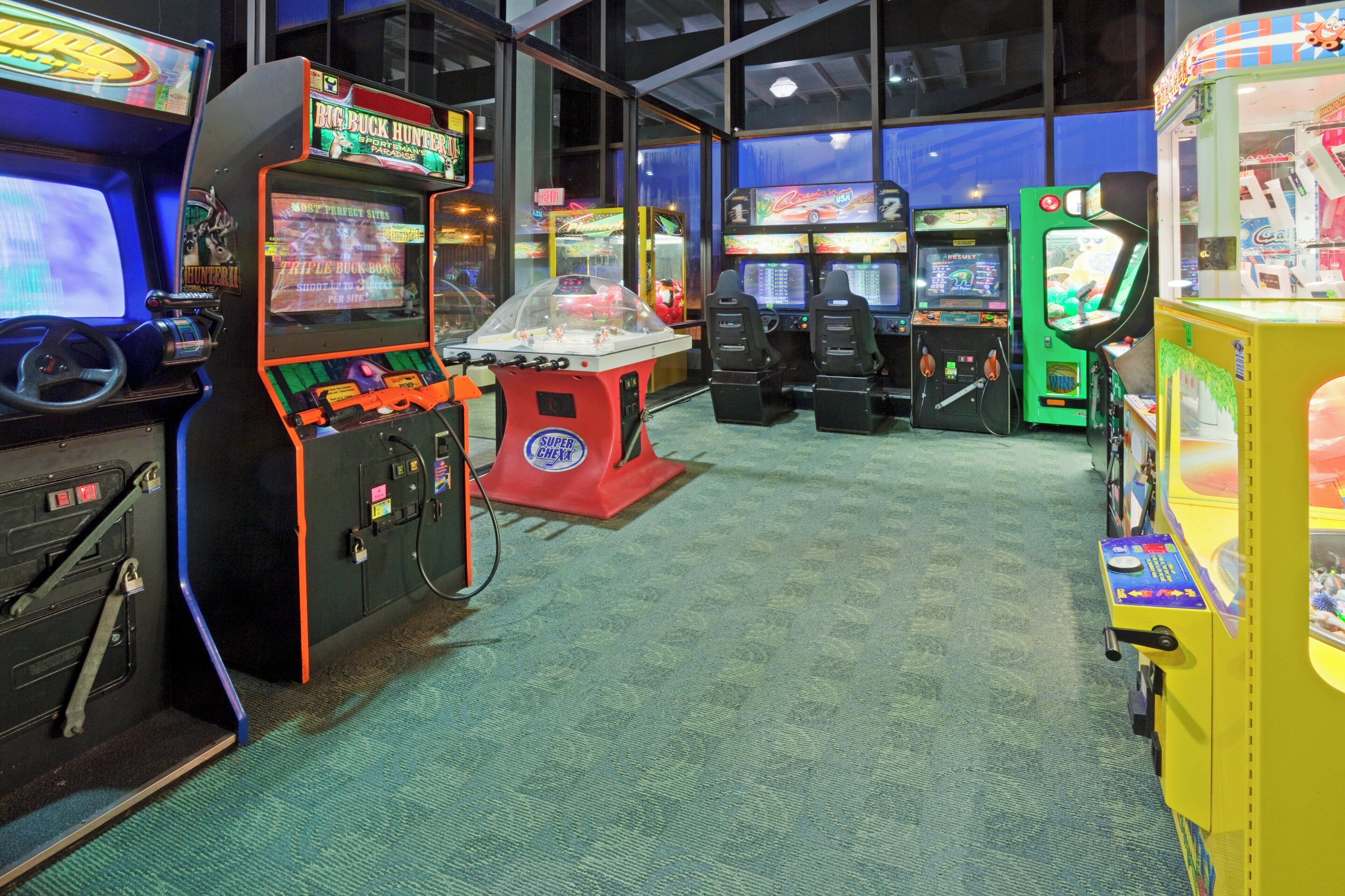 Una fila de juegos de arcade en una habitación con piso alfombrado y ventanas amplias.