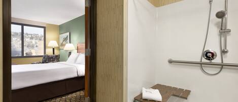 A hotel room with a bed, a window with a view, a shower with a handrail, and a towel rack.