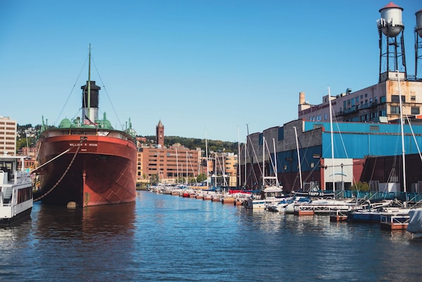 Un grand navire rouge était amarré dans une marina, avec de plus petits bateaux et des bâtiments en arrière-plan.