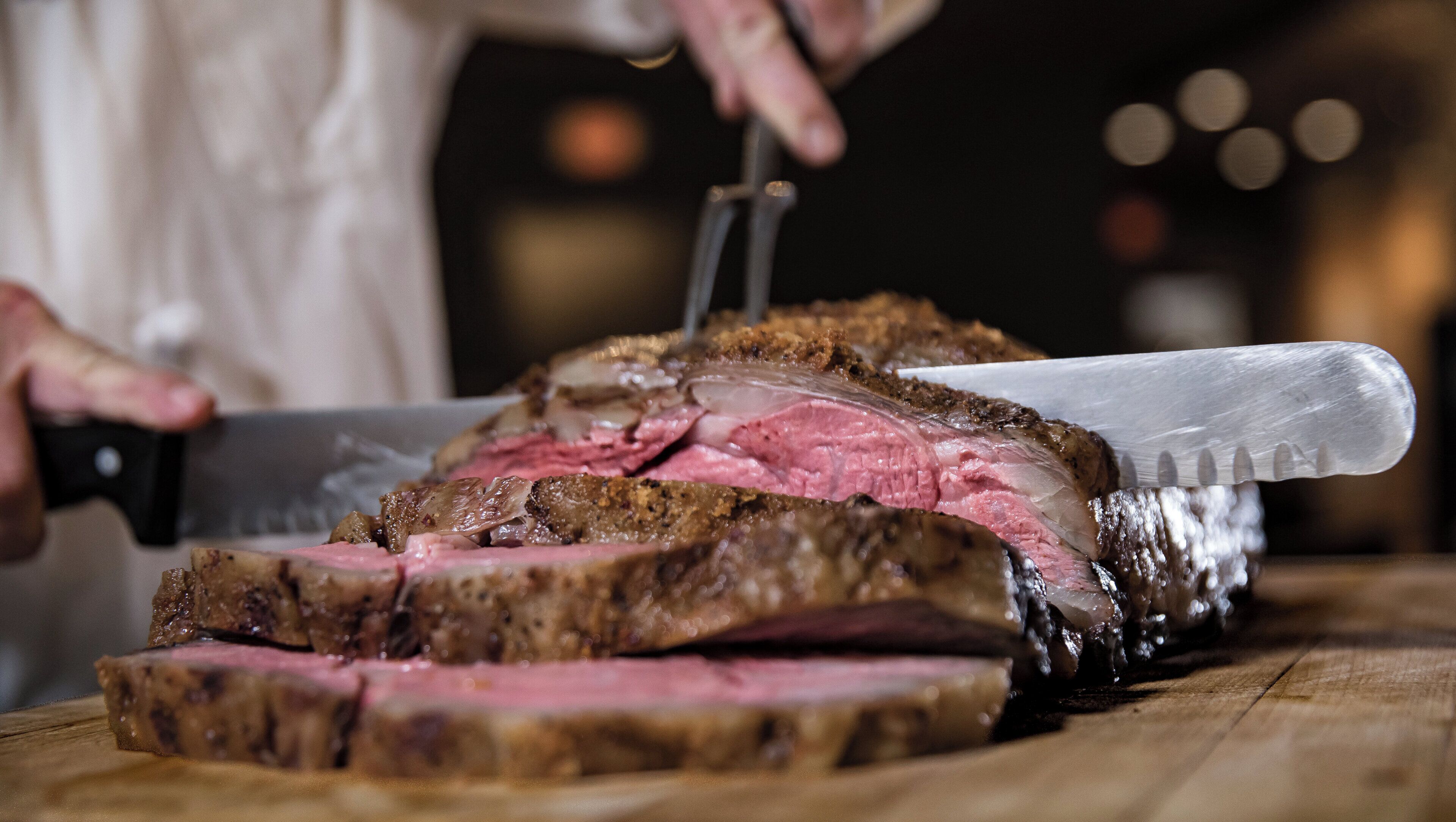 Una persona che affetta una preparazione a base di carne su un tagliere di legno.
