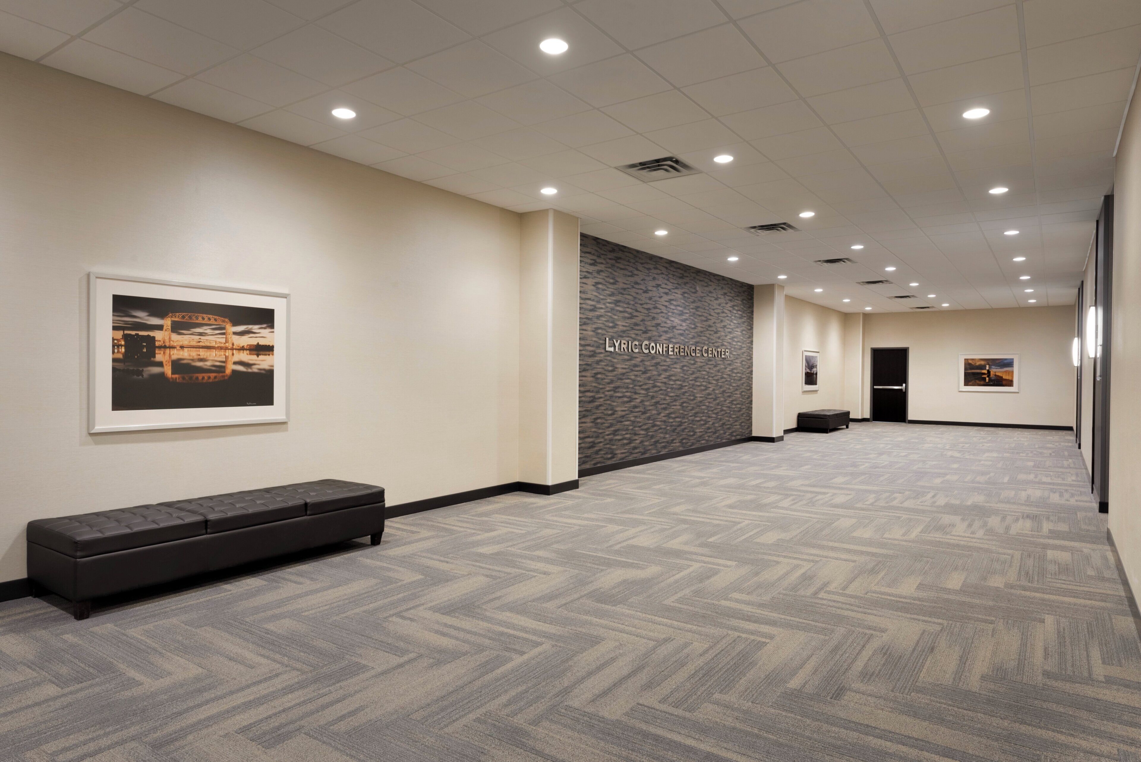 A hallway with a patterned carpet, a bench, and a wall with a textured design and the text 'LYRIC CONFERENCE CENTER'.