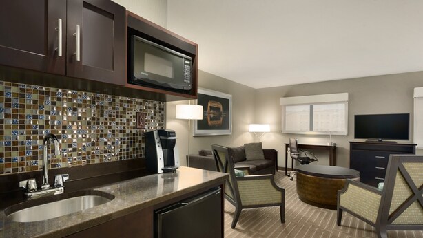 A modern kitchen with a built-in microwave, a coffee maker, and a sink. There is a dining area with a round table and chairs. - Holiday Inn & Suites Duluth Downtown by IHG (Duluth)