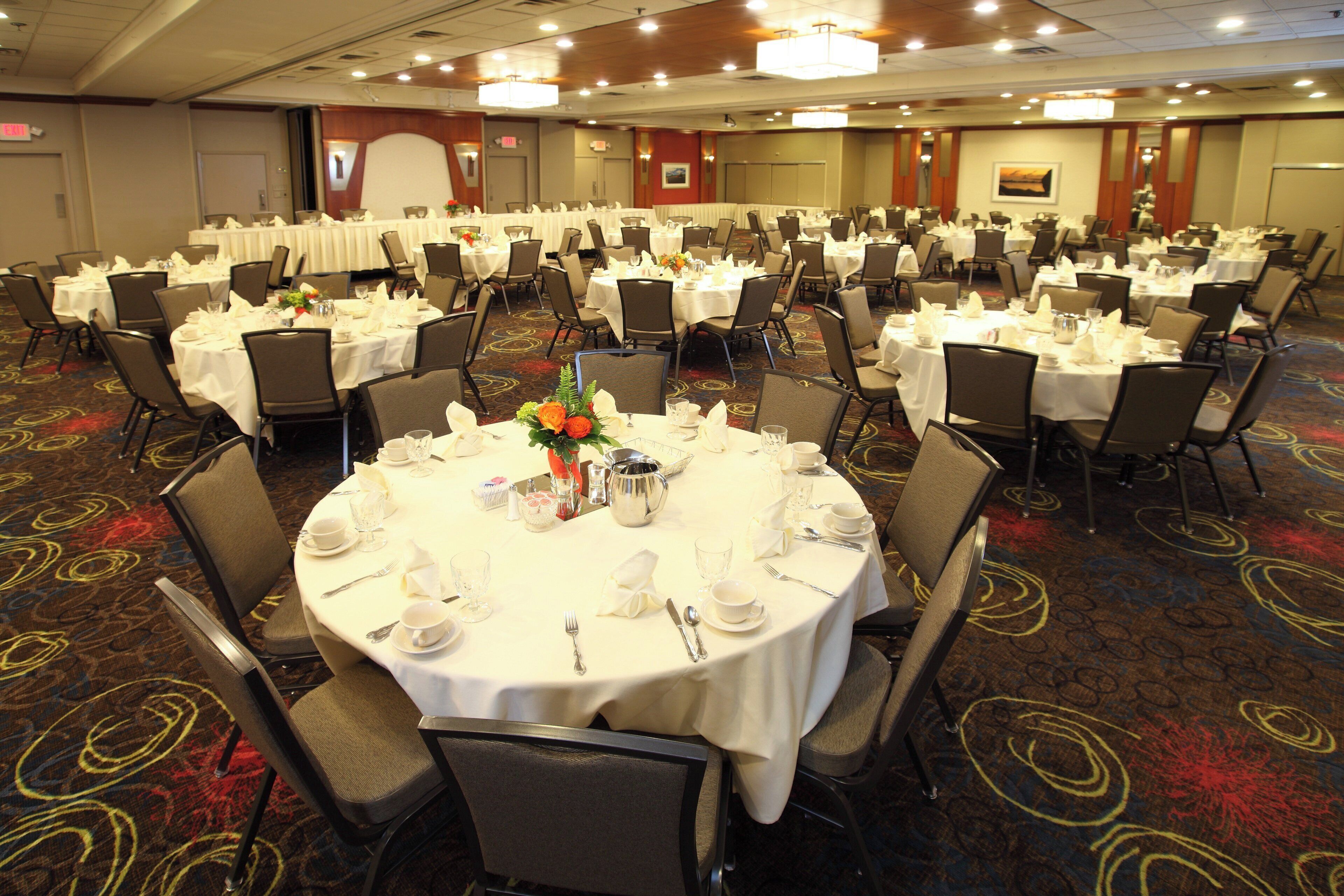 A banquet hall with round tables set for dining, equipped with chairs, tablecloths, and centerpieces.