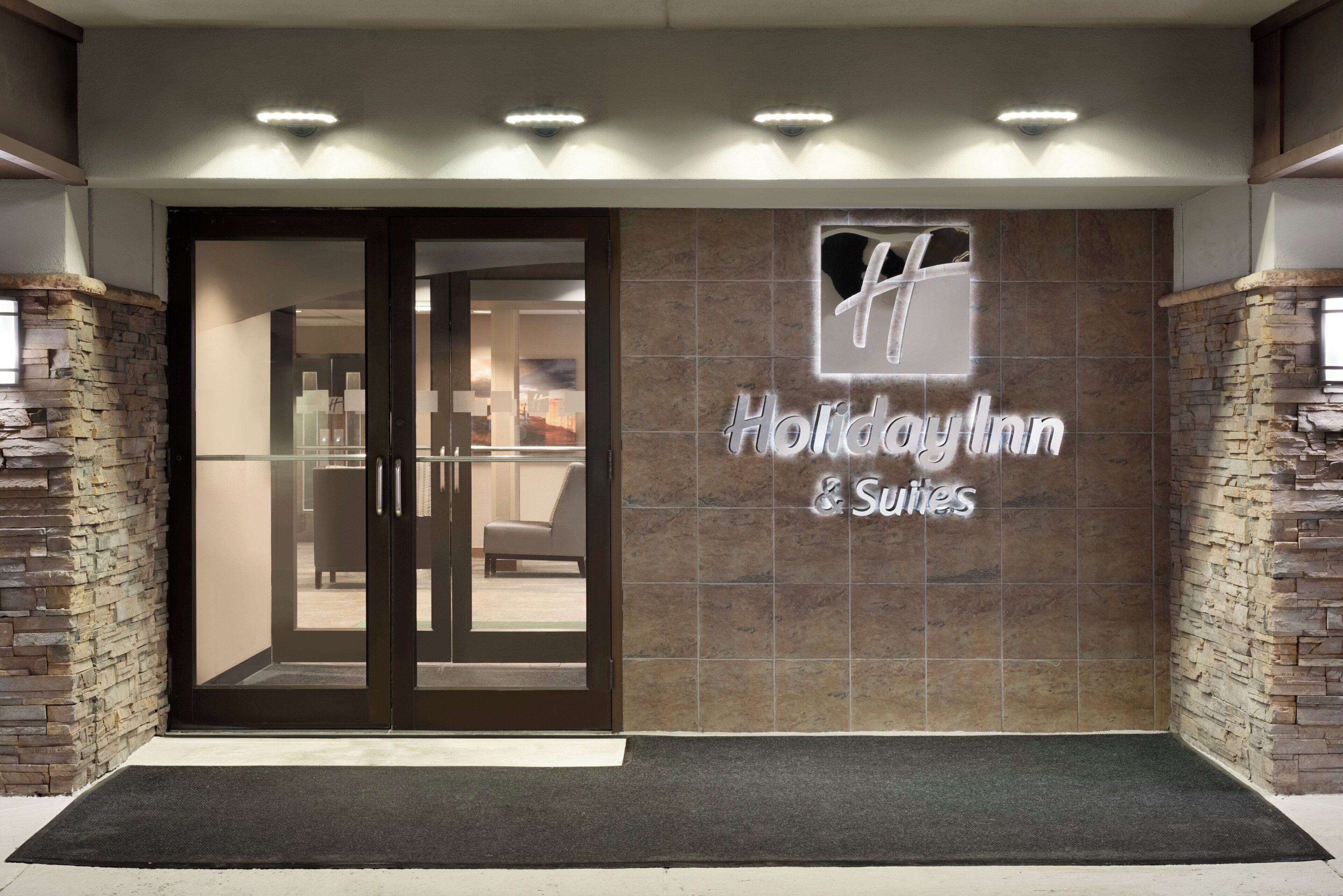 A hotel entrance with a stone facade, a glass door, and a sign reading 'Holiday Inn & Suites'.