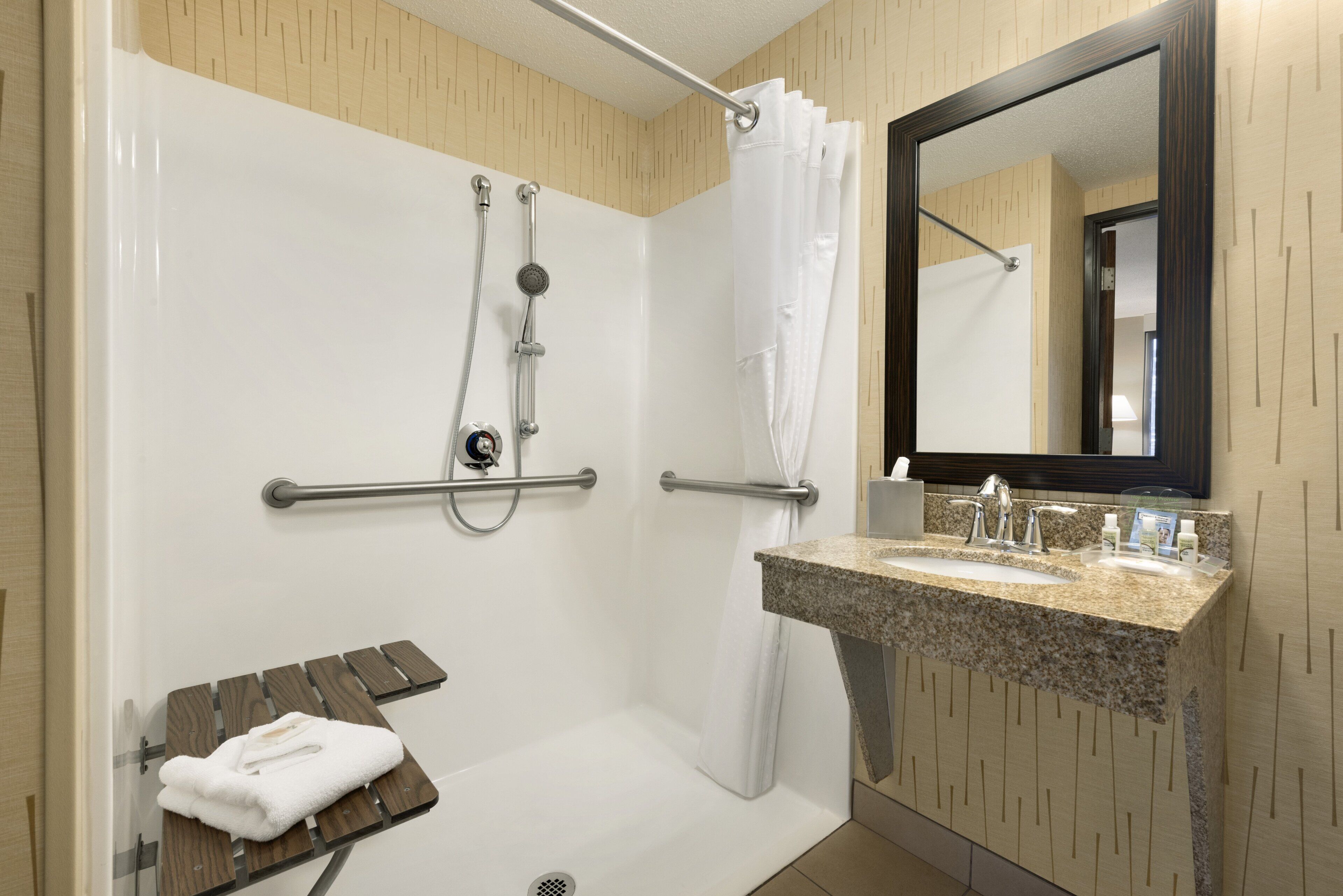 A modern bathroom with a shower, grab bars, a bench, and a sink with a mirror.
