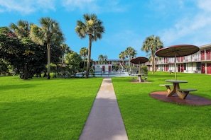 A hotel courtyard with a pool, palm trees, and outdoor seating. - HomeTowne Studios By Red Roof Vero Beach - I-95 (Vero Beach)