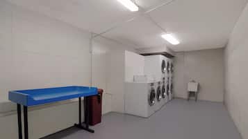 A laundry room with a blue table, a red trash bin, and a row of washing machines.