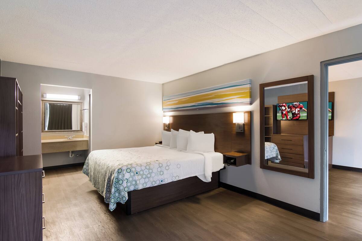 A modern hotel room with a large bed, a bedside table, a mirror, and a television.