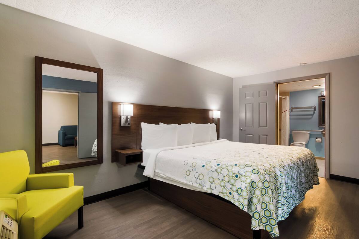 A hotel room with a bed, a mirror, a bedside table, a lamp, and a chair.