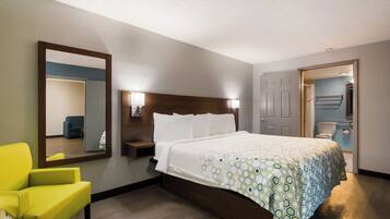 A hotel room with a bed, a mirror, a nightstand, a chair, and a door leading to a bathroom.