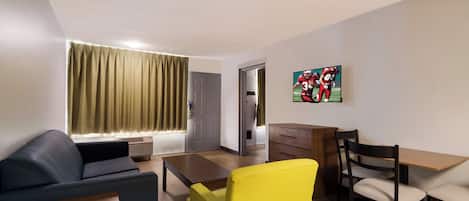 Ein Wohnzimmer mit einer Couch, einem gelben Sessel, einem Holztisch und einem an der Wand befestigten Fernseher.