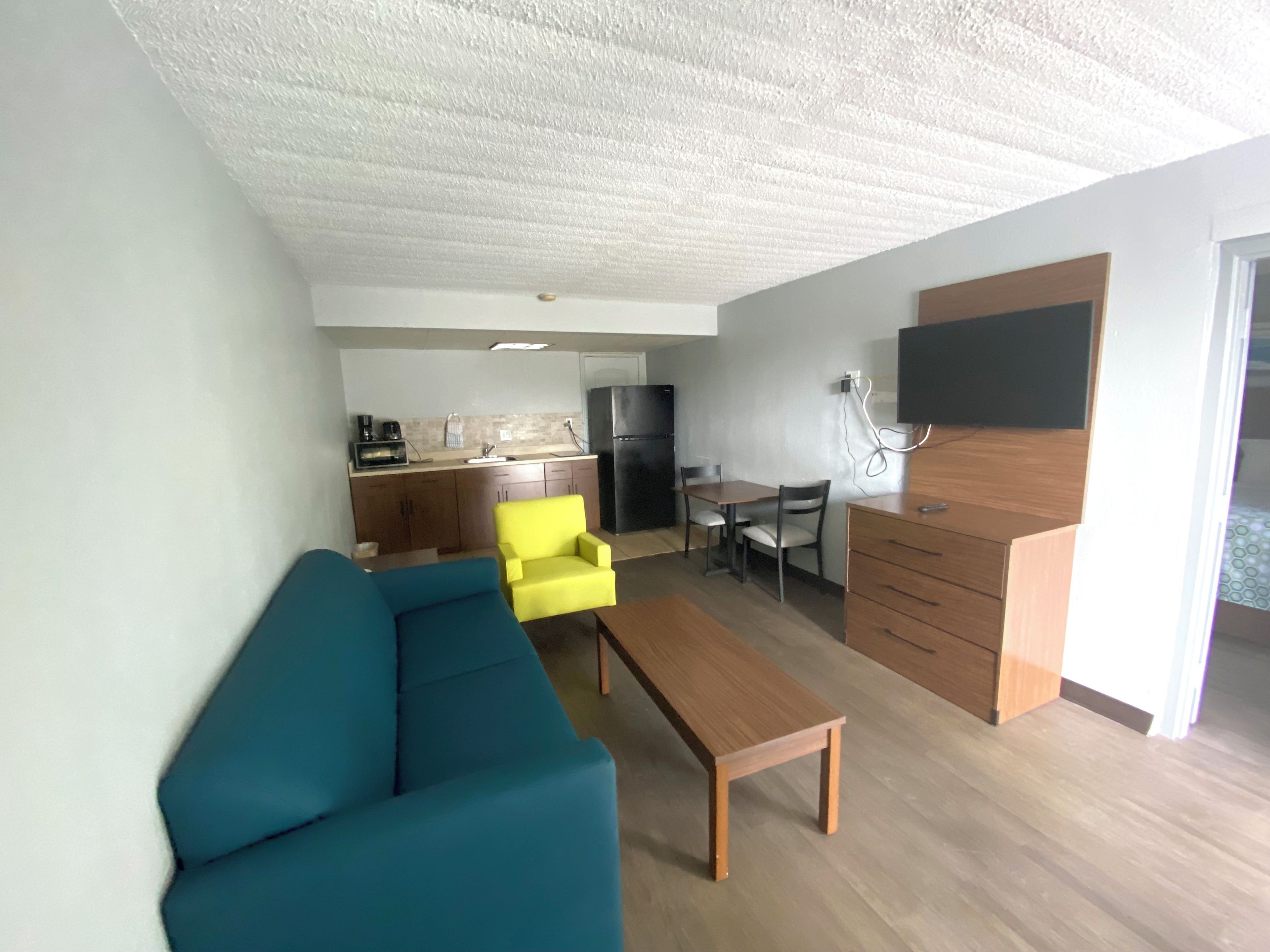 Un espacio habitable compacto con sofá, una mesa baja, una mesa de comedor con sillas, zona de cocina y un televisor de pantalla plana montado en la pared.