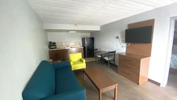 Un espacio habitable compacto con sofá, una mesa baja, una mesa de comedor con sillas, zona de cocina y un televisor de pantalla plana montado en la pared.