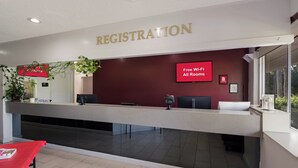 Zona de recepción de un hotel con un mostrador de registro, un cartel que indica conexión Wi-Fi gratuita y una ventana con vistas al exterior.