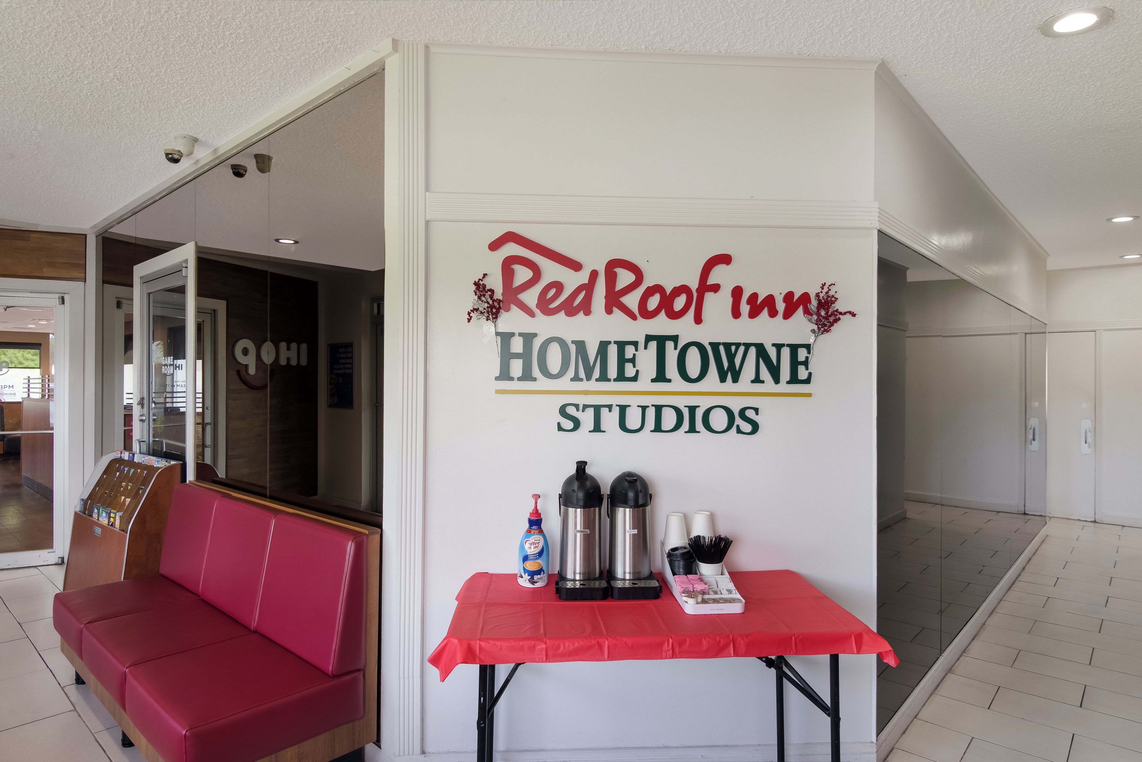 Schild eines RedRoof Inn HOME TOWNE STUDIOS mit einem Tisch, auf dem Kaffeegeräte stehen, und einer roten Bank.