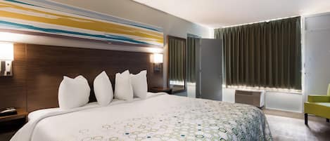Habitación de hotel con una cama grande, cabecera de madera, lámpara de pared, ventana con cortinas y mesita de noche con lámpara.
