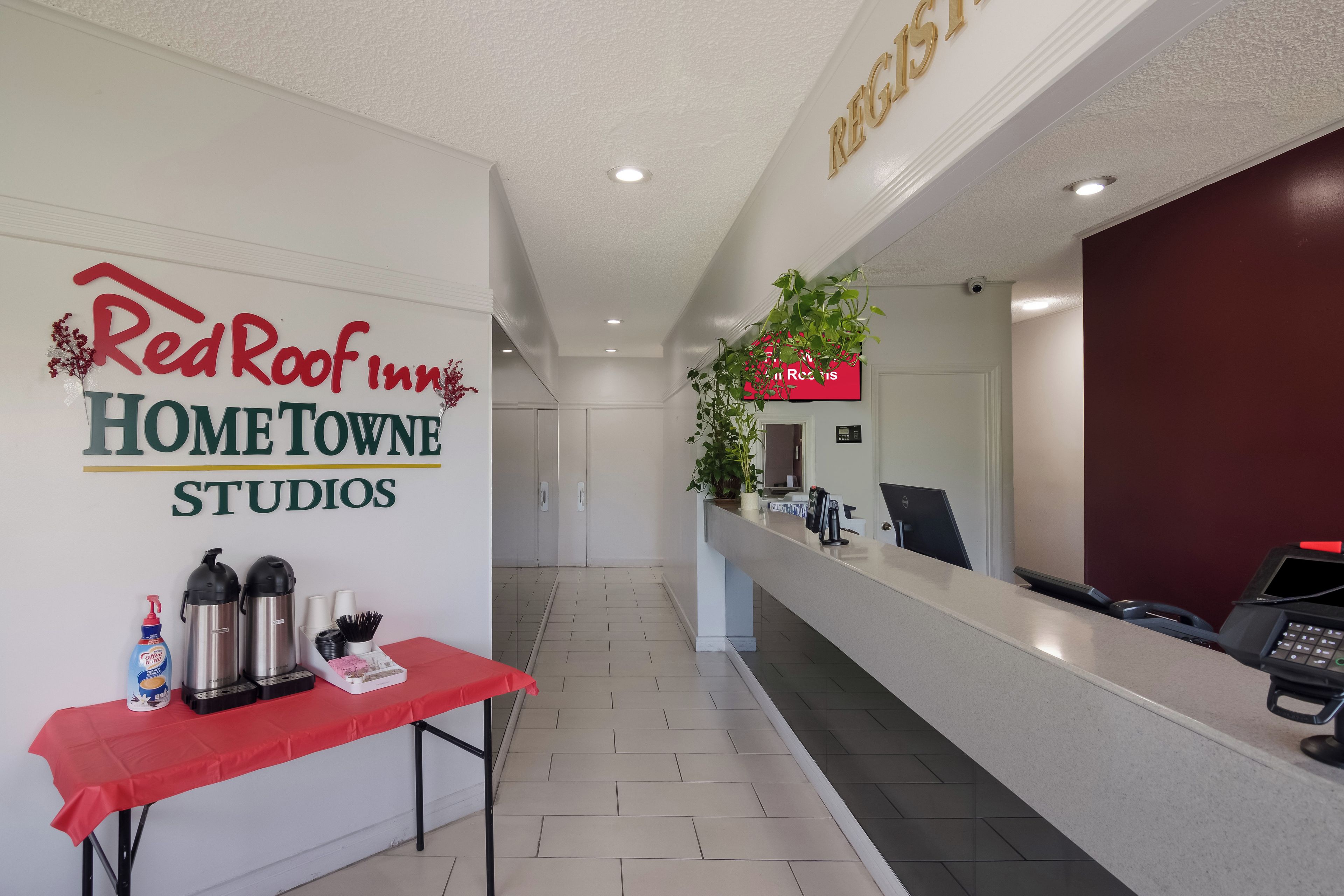 Ein Empfangsbereich mit einem Red Roof Inn Schild, einem Empfangsschalter, einer Kaffeestation und einer Pflanze.
