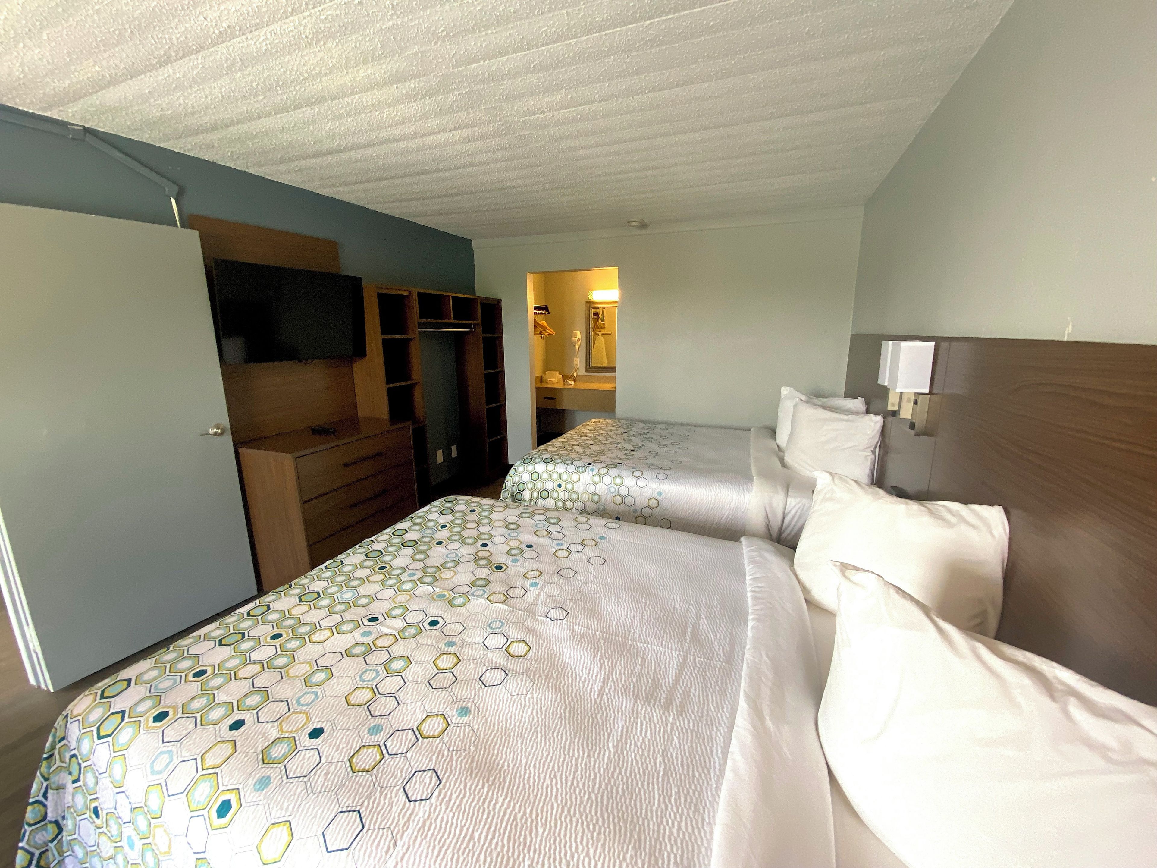 A hotel room with two beds, a TV, a wardrobe, and a bathroom visible in the background.