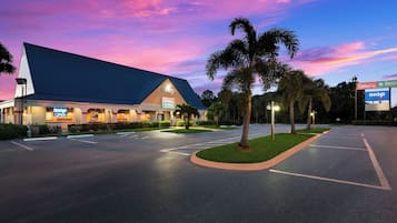 Um hotel com uma placa grande, estacionamento e palmeiras.