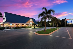 A hotel with a large sign, a parking lot, and palm trees. - HomeTowne Studios By Red Roof Vero Beach - I-95 (Vero Beach)