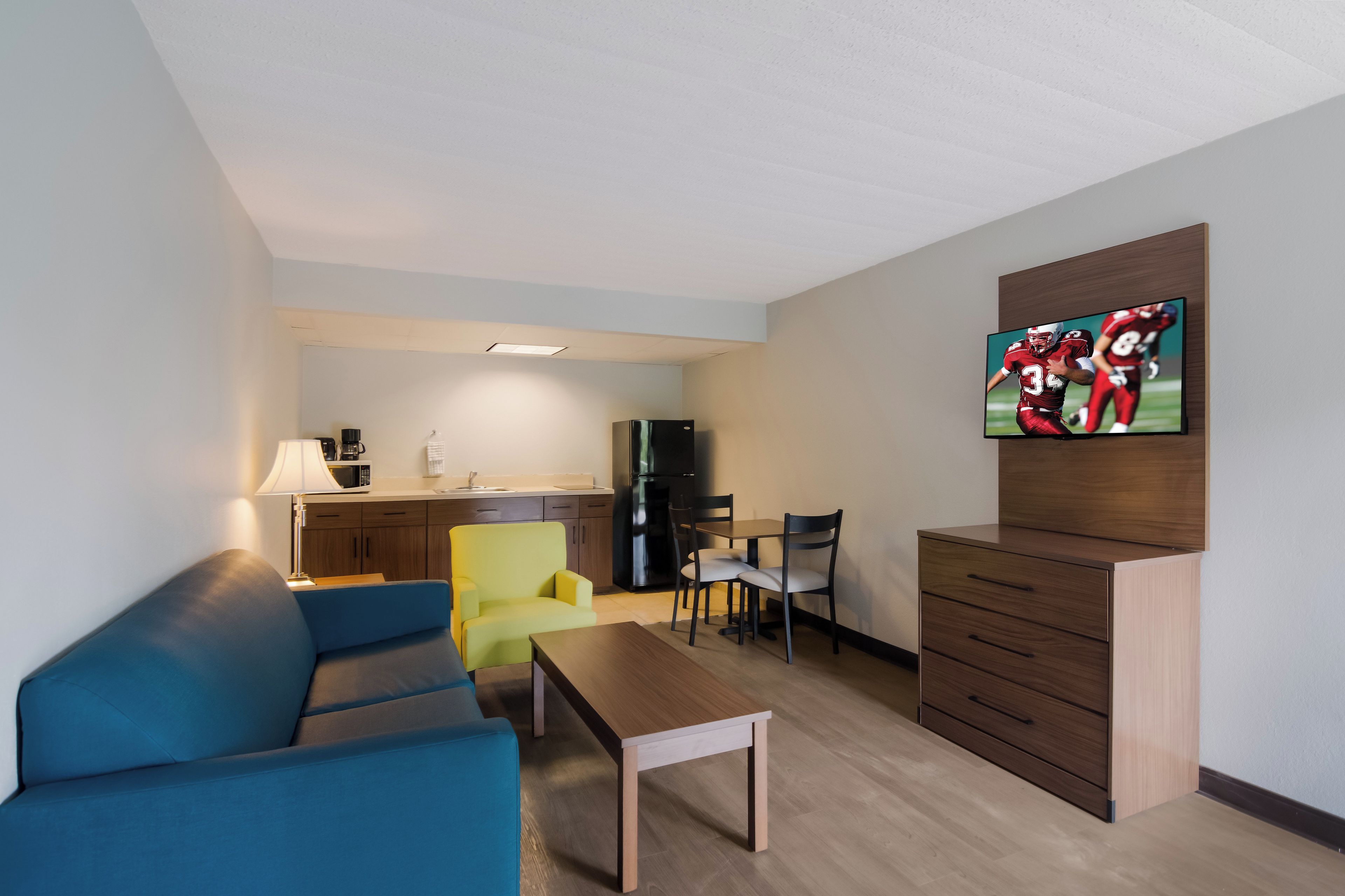 Un espacio habitable compacto con kitchenette, una zona de comedor con sillas, un sofá y un televisor montado en la pared.