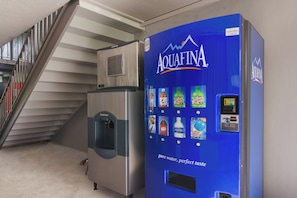 A water dispenser with a blue label and a beverage vending machine with various drink options. - HomeTowne Studios By Red Roof Vero Beach - I-95 (Vero Beach)