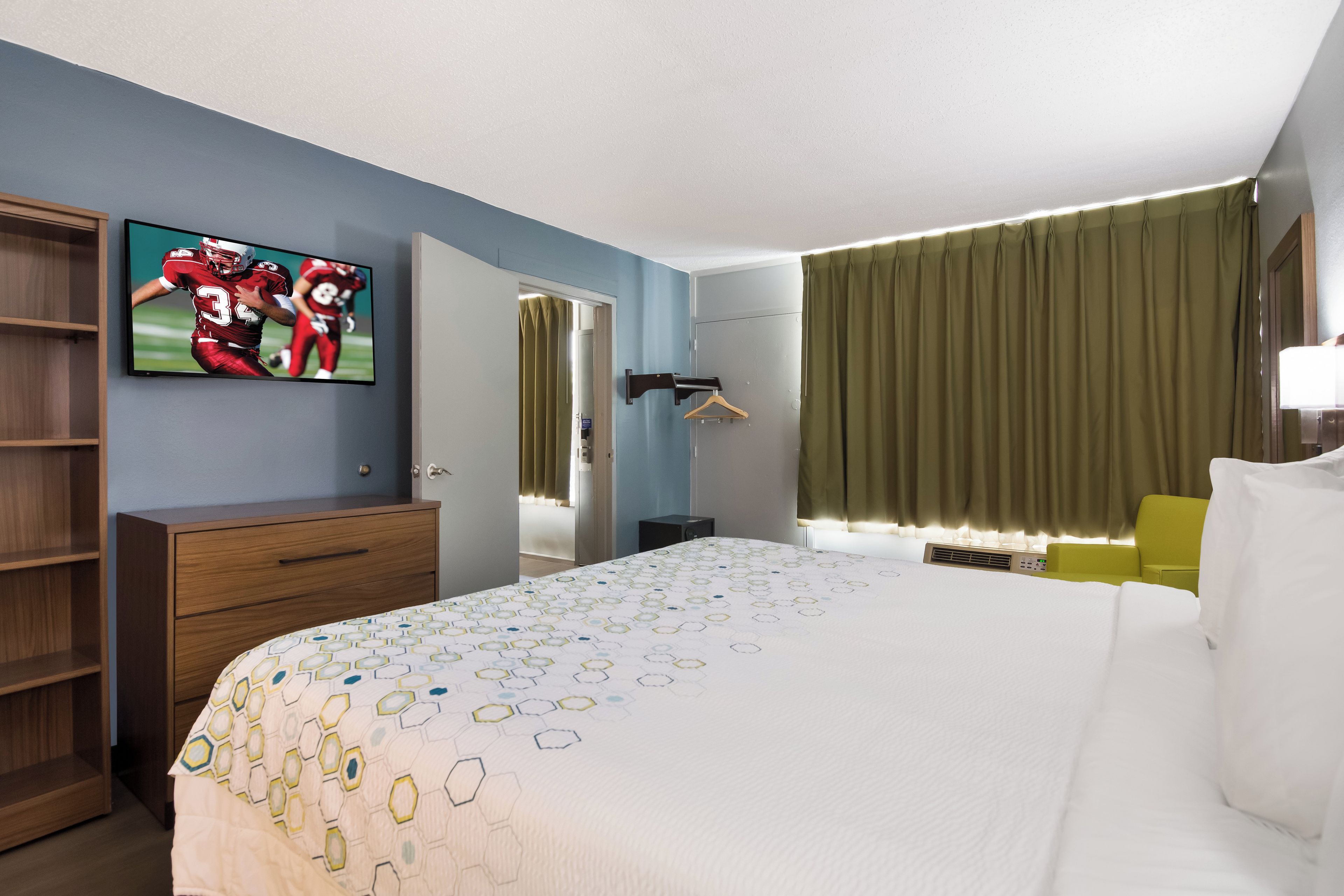 A hotel room with a bed, a television, a wardrobe, a desk, and a window with curtains.