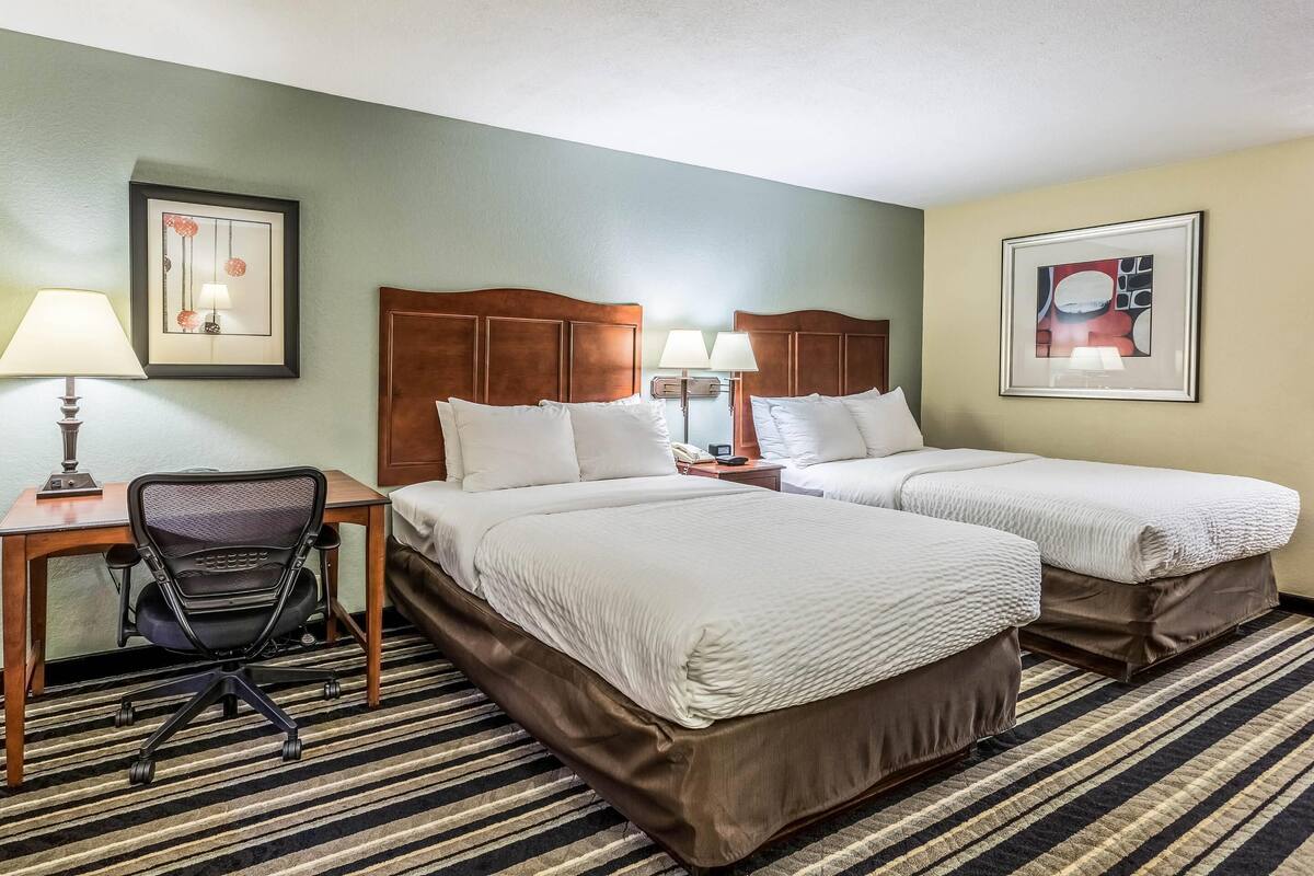 A hotel room with two beds, a desk, a chair, and two bedside tables with lamps.