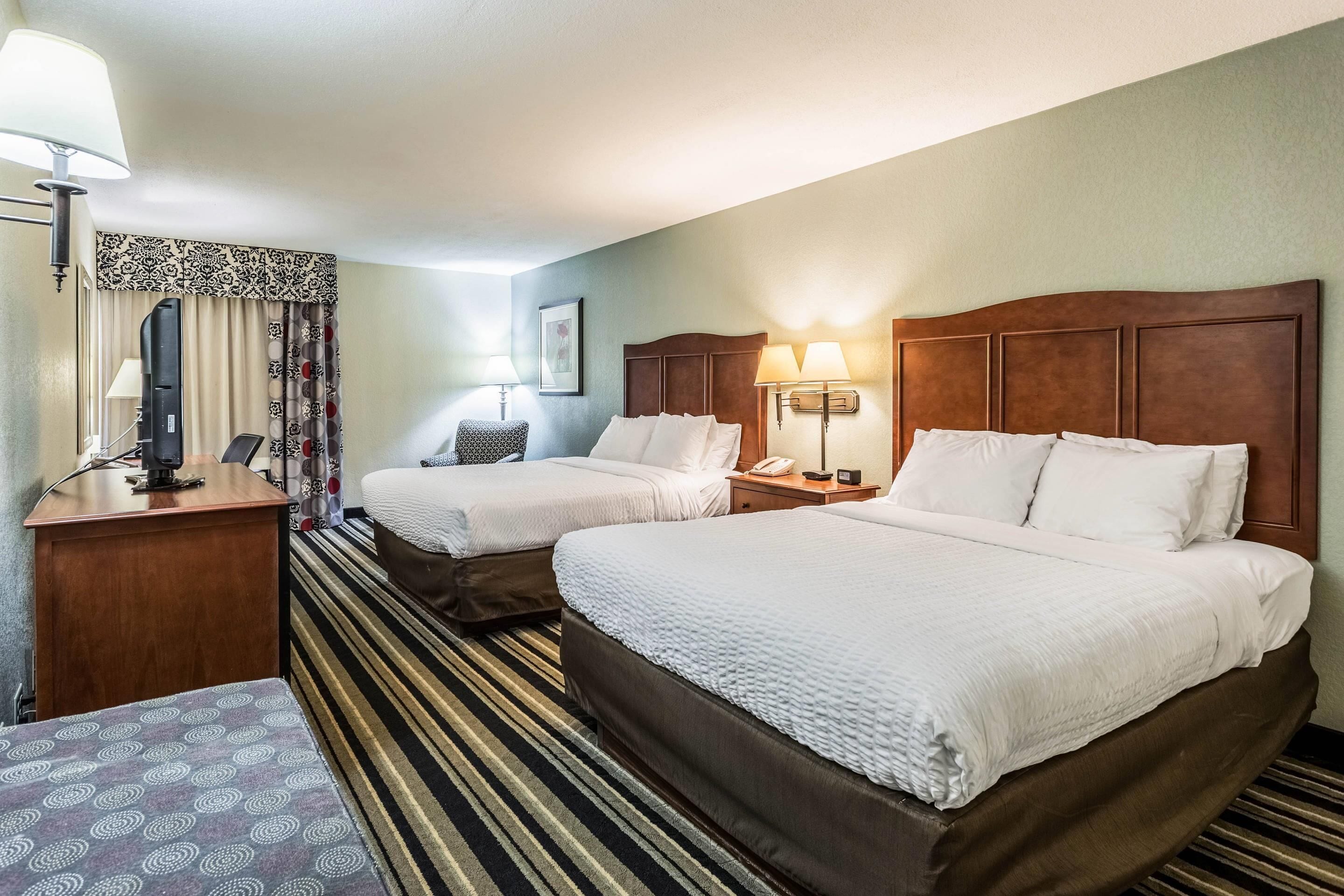 Une chambre d’hôtel avec deux lits simples, un bureau avec un ordinateur, une chaise et un tapis à rayures.