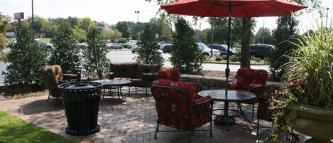 An outdoor patio area with brick flooring, red and black outdoor furniture, and a red umbrella.