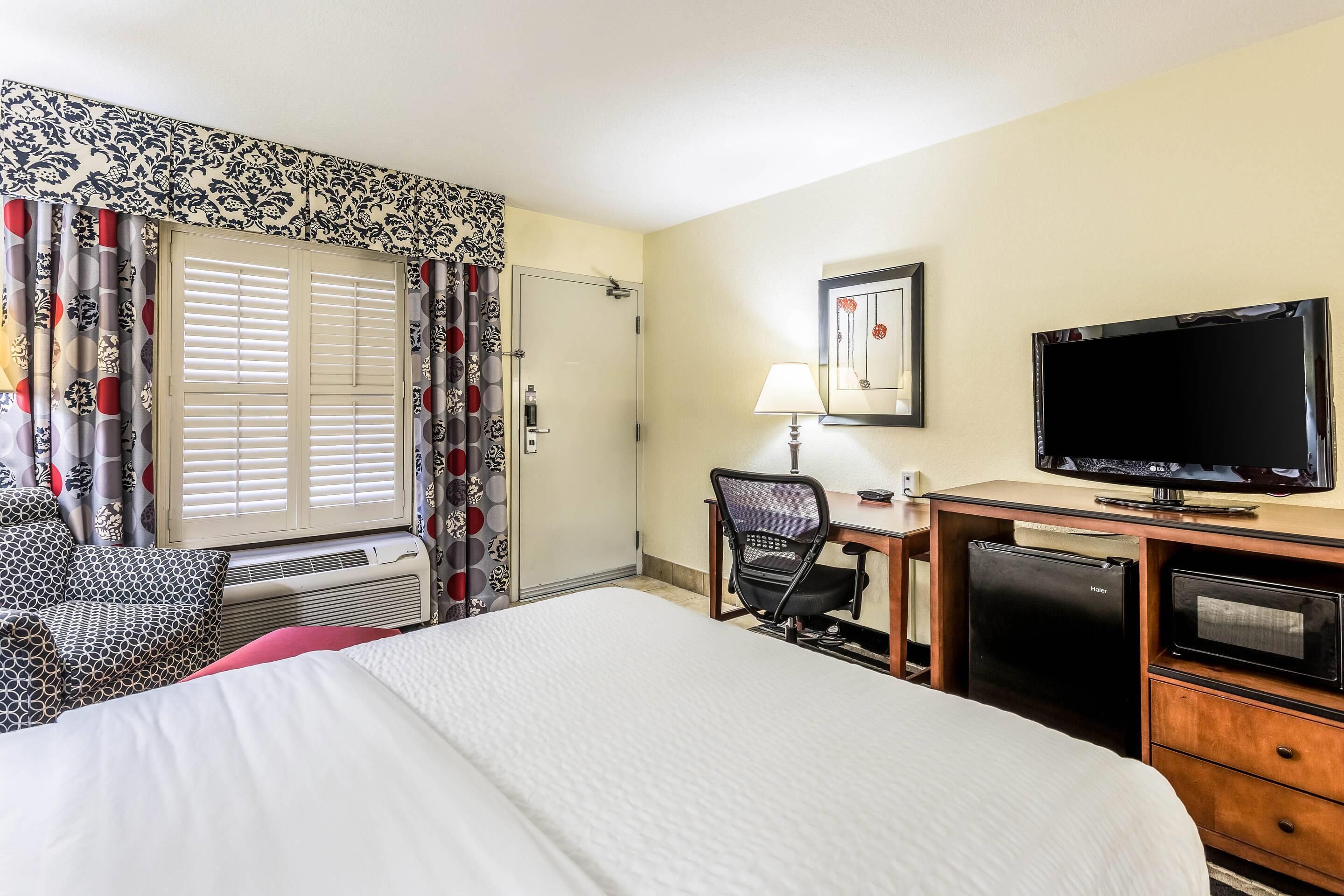 Una habitación de hotel con una cama grande, un escritorio con computadora, televisión y un mini bar.